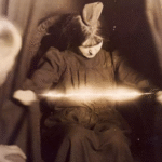 Médium de efecto físico manifestando energía espiritual, con rayos de luz visibles entre sus manos, mientras una persona observa atentamente.