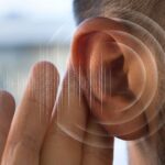 Imagen en primer plano de un oído humano con ondas sonoras digitales ilustradas alrededor, representando la percepción auditiva o la detección de sonidos sutiles